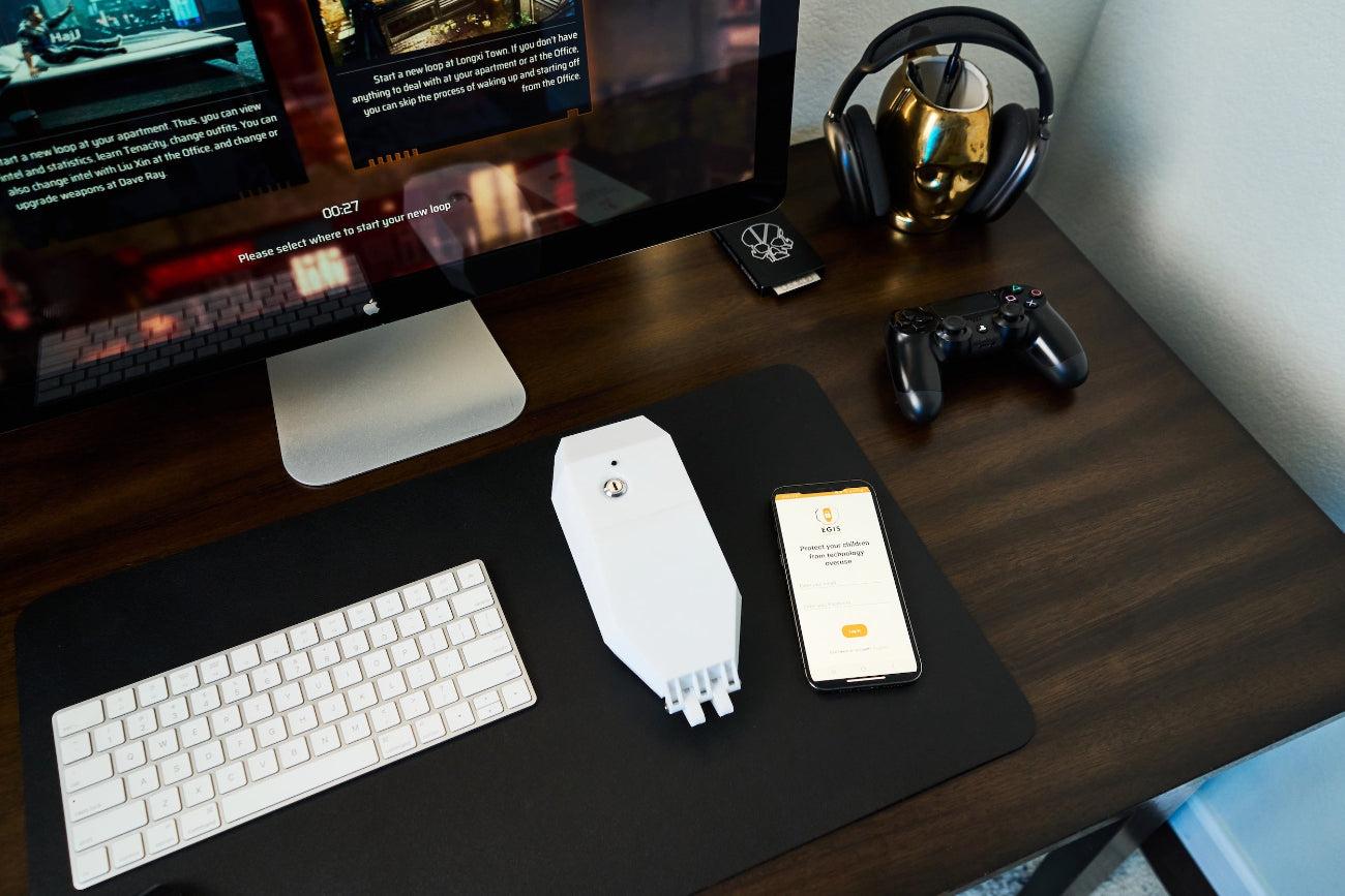 Image of locking smart plug device alongside app sitting on wook desk with montior.
